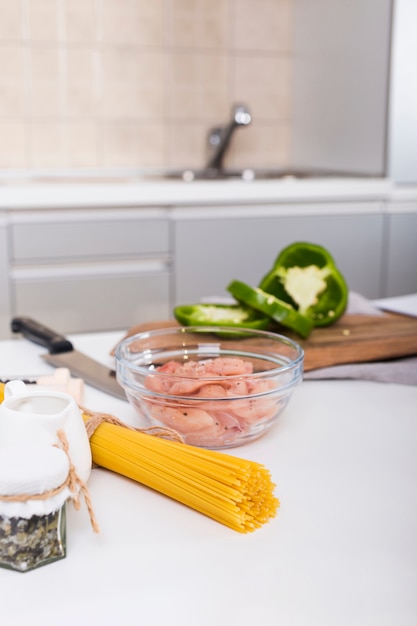 Photo gratuite spaghettis crus; poulet dans un bol et tranches de poivron sur la table