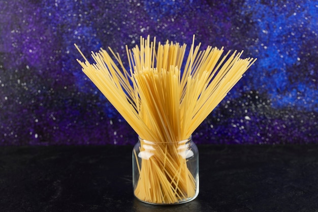 Spaghettis secs crus dans un bocal en verre sur une table lumineuse.