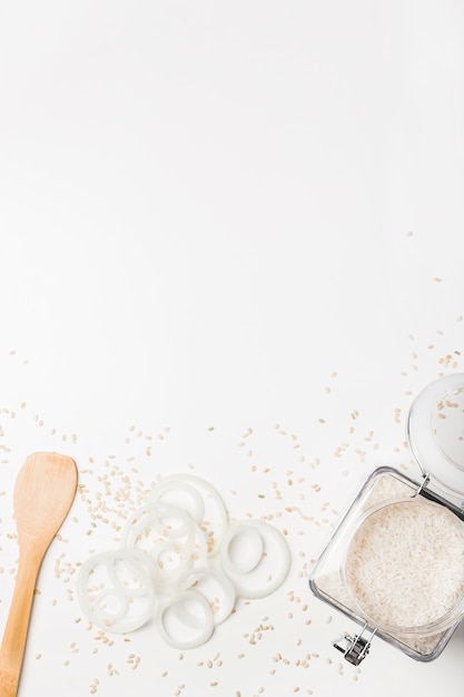 Photo gratuite spatule; rondelles d'oignon et pot de riz sur une surface blanche