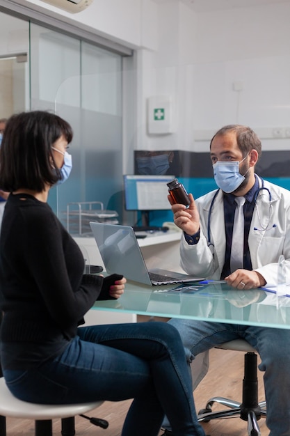 Spécialiste donnant une bouteille de pilules sur ordonnance au patient pour traitement, faisant une consultation de contrôle dans le cabinet. Femme recevant un flacon de médicaments d'un médecin pendant la pandémie de covid 19.