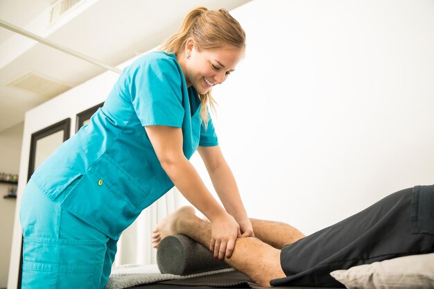 Spécialiste en physiothérapie souriant donnant un massage au patient pour soulager la douleur du mollet à l'hôpital