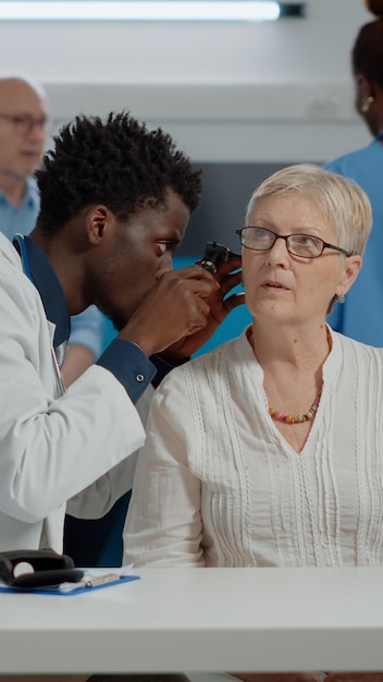 Spécialiste de la santé tenant un otoscope professionnel pour l'examen de l'oreille d'un patient âgé au bureau du bureau du médecin. Otologue utilisant un outil sur une femme âgée de race blanche infectée à la clinique