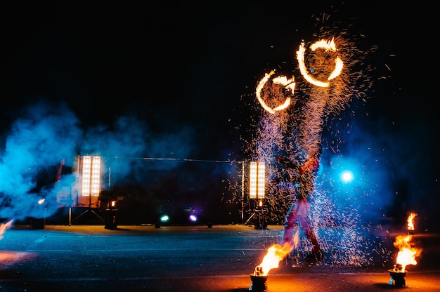 Spectacle de feu, danse avec la flamme, maître masculin jonglant avec des feux d'artifice, performance en plein air, dessine une silhouette enflammée dans l'obscurité, des étincelles lumineuses dans la nuit. un homme en costume led danse avec le feu.