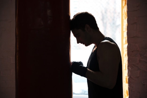 Sportif homme fatigué s'appuyant sur un sac de frappe pendant l'entraînement