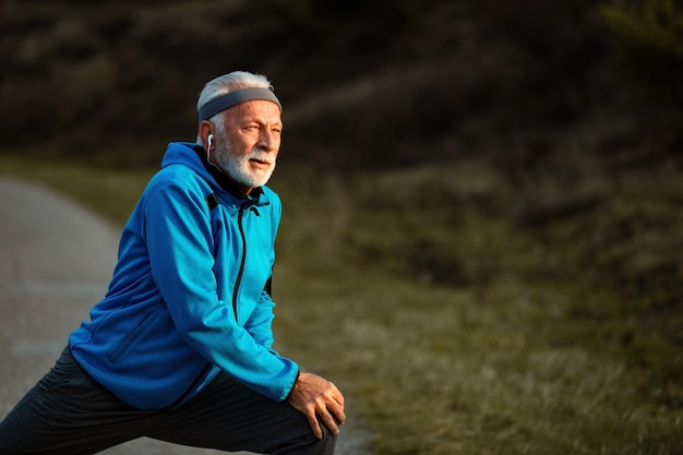 Sportif senior actif faisant des exercices d'étirement et d'échauffement avant l'entraînement sportif dans la nature Espace de copie