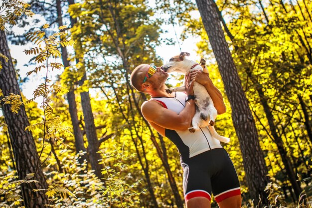 Sportif en vêtements de sport et lunettes de soleil avec son petit chien dans la forêt verte.