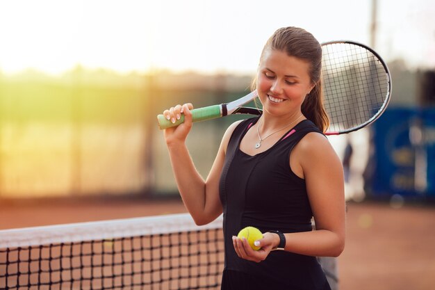 Sportive belle fille regardant la balle de tennis, debout sur le terrain avec une raquette.