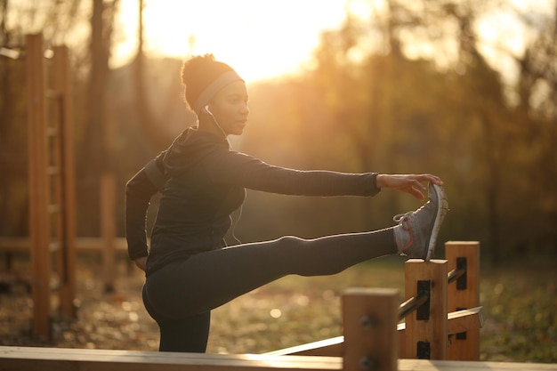 Sportive noire faisant des exercices d'étirement tout en s'échauffant dans la nature au coucher du soleil