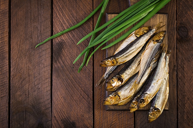 Sprat fumé et oignon vert sur une planche à découper. Poisson fumé. Vue de dessus