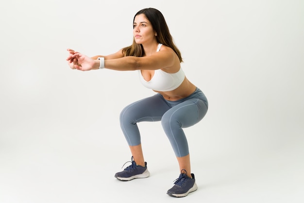 Les squats sont le meilleur exercice pour vos jambes. Femme mince de forme physique dans des vêtements de sport faisant une séance d'entraînement de squat sur un fond blanc.