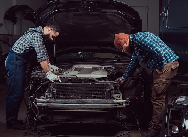 Photo gratuite station-service. deux mécaniciens brutaux barbus réparant une voiture dans le garage.