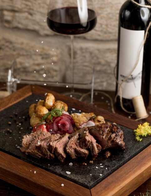 Steak de boeuf finement coupé avec pommes de terre bouillies et herbes, et un verre de vin rouge