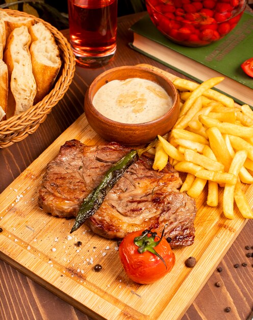 Steak de boeuf avec frites, sauce mayonnaise à la crème sure et herbes sur une assiette en bois