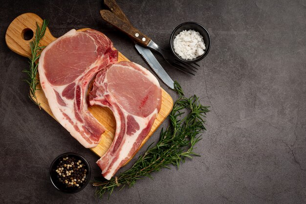 Steak de côtelette de porc cru sur la surface sombre.