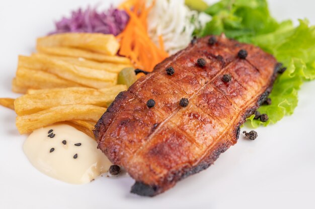 Steak de poisson avec frites, kiwi, laitue, carottes, tomates et chou dans un plat blanc.