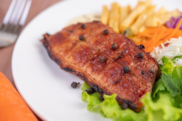 Steak de poisson avec frites, kiwi, laitue, carottes, tomates et chou dans un plat blanc.