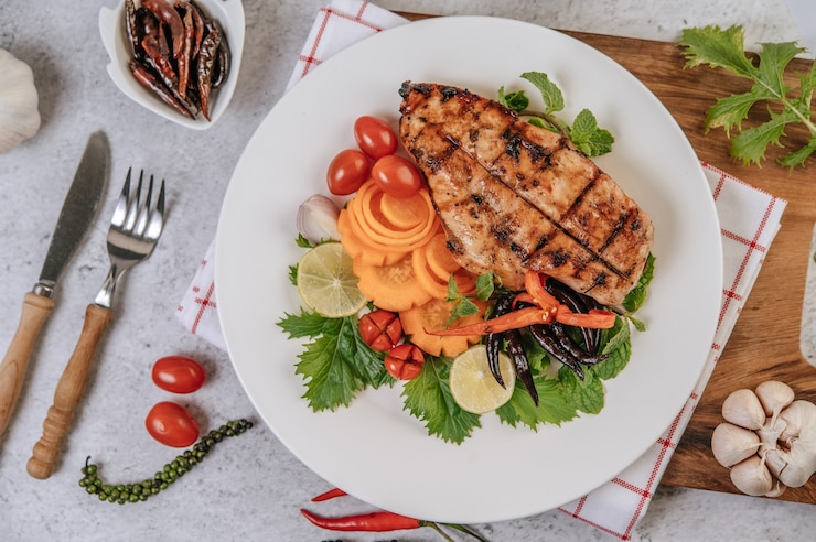 Photo gratuit steak de poulet au citron, tomate, chili et carotte sur plaque blanche.