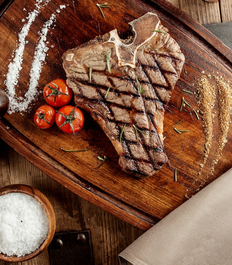 Photo gratuit steak t-bone grillé servi avec des herbes salées et des tomates cerises grillées