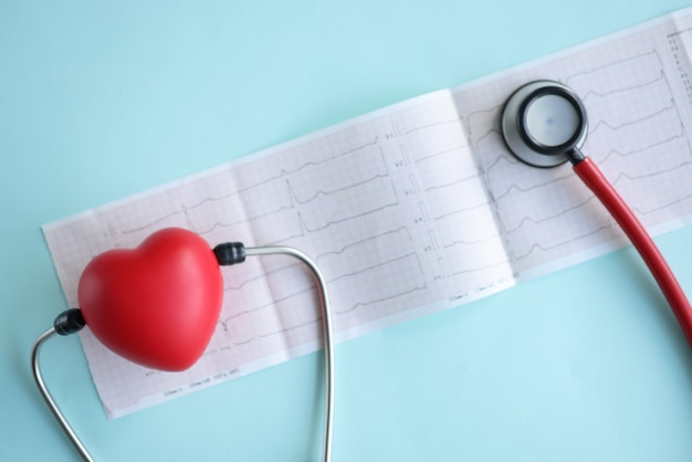 Stéthoscope et coeur rouge de jouet se trouvant sur l'électrocardiogramme sur le plan rapproché bleu de fond