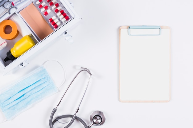 Photo gratuite stéthoscope; masque chirurgical et presse-papiers avec trousse de premiers soins sur fond blanc