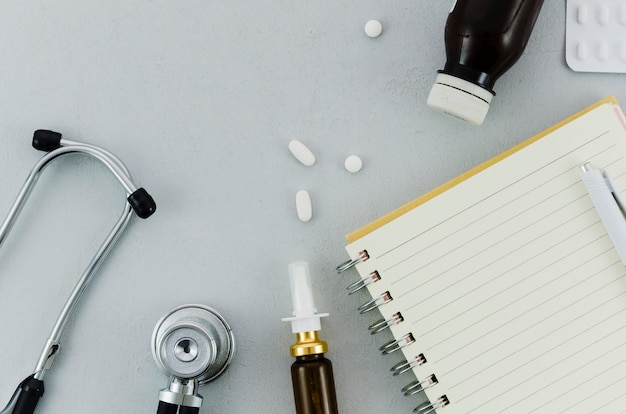 Stéthoscope; des pilules; bouteille; spray nasal; Journal et stylo sur fond gris