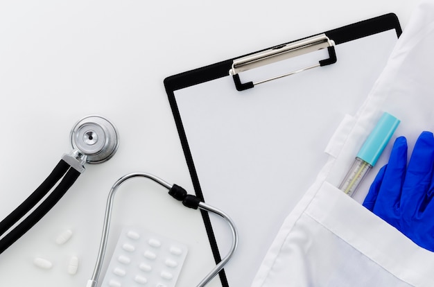 Stéthoscope; des pilules; presse-papiers; thermomètre; gants bleus en poche sur fond blanc