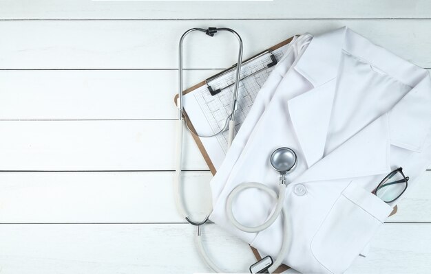 Le stéthoscope, le presse-papiers et l&#39;uniforme du médecin sur le bureau blanc en bois pur