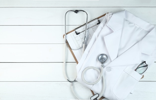 Photo gratuite le stéthoscope, le presse-papiers et l'uniforme du médecin sur le bureau blanc en bois pur