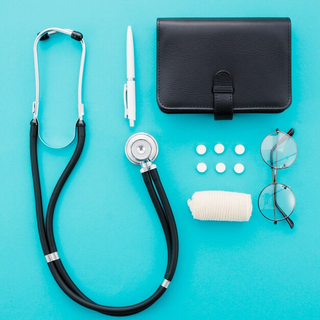 Stéthoscope; stylo; des pilules; journal intime; lunettes et bandage sur fond bleu