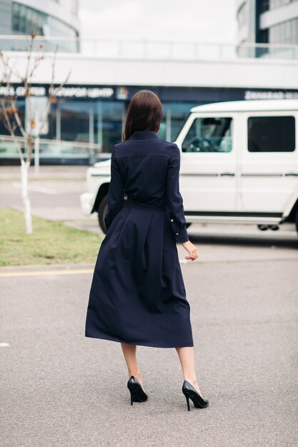 Stock photo d'une femme brune méconnaissable en robe noire en coton avec jupe longue et talons en cuir noir debout dans la rue.