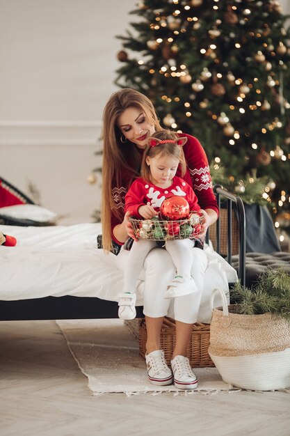 Stock photo de mère aimante en robe verte donnant sa petite fille en pyjama robe un cadeau de Noël. Ils sont à côté d'un arbre de Noël joliment décoré sous la neige.