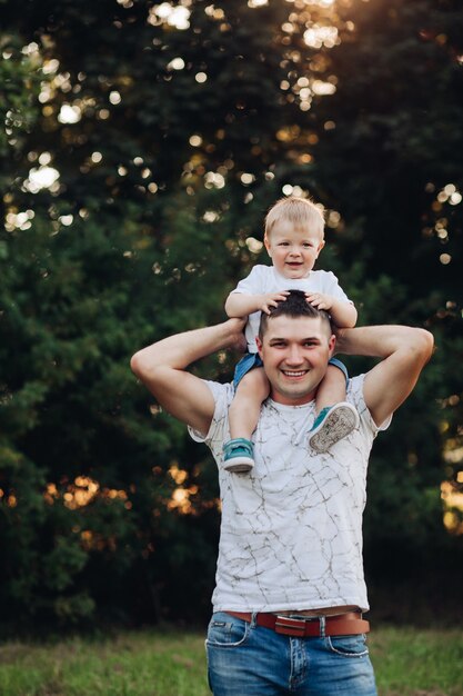 Stock photo d'un père aimant tenant son bébé sur les épaules. Beau garçon souriant assis sur les épaules de papa dans un parc d'été verdoyant.