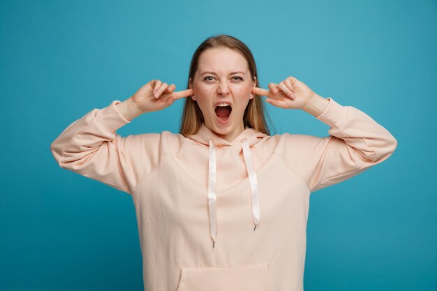 Stressé jeune femme blonde mettant les doigts dans les oreilles en hurlant