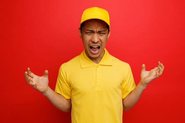 Stressé jeune livreur portant casquette et uniforme montrant les mains vides hurlant