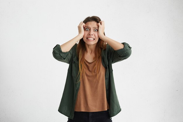 Stressée anxieuse jeune femme habillée avec désinvolture, déchirant les cheveux, ressentant la tension et le stress tout en faisant face à des problèmes, ne peut pas supporter la pression, serrant les dents et gardant les yeux ouverts.