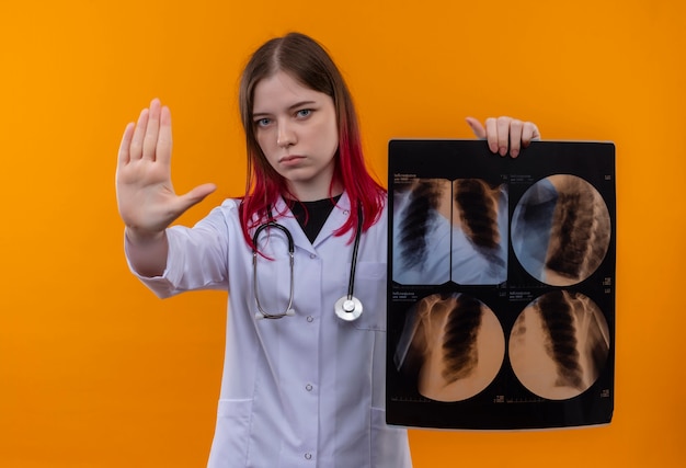 Strict young doctor girl wearing stéthoscope robe médicale holding x-ray montrant le geste d'arrêt sur fond orange isolé