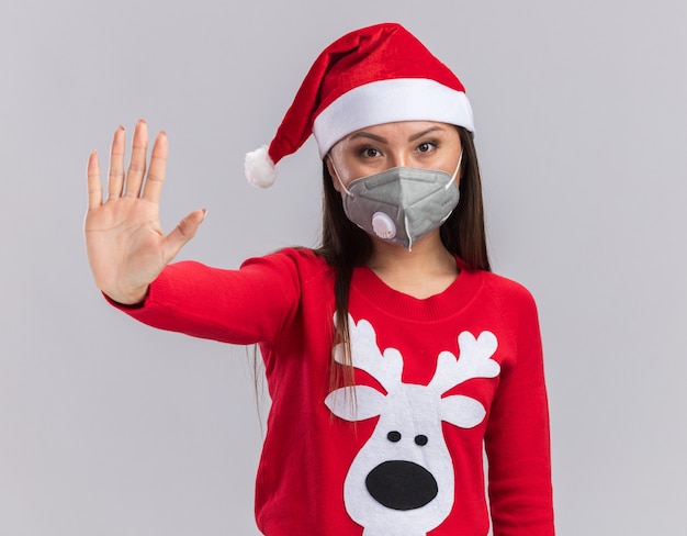 Stricte jeune fille asiatique portant chapeau de Noël avec pull et masque médical montrant le geste d'arrêt isolé sur fond blanc