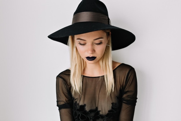 Photo gratuite studio portrait en gros plan d'une jolie femme aux lèvres sombres porte un chapeau et un chemisier regarde vers le bas sur fond isolé