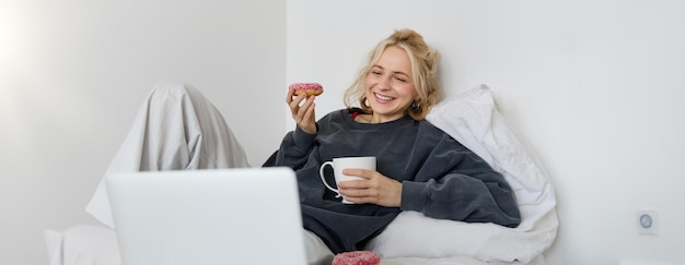 Photo gratuite style de vie et concept de personnes femme blonde heureuse allongée dans le lit avec de la nourriture buvant du thé et mangeant
