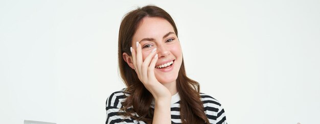Photo gratuite style de vie heureuse jeune femme riant en touchant son visage et souriant à la caméra fond blanc