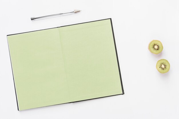 Stylo sur le dessus d&#39;un cahier ouvert avec kiwi coupé en deux isolé sur fond blanc