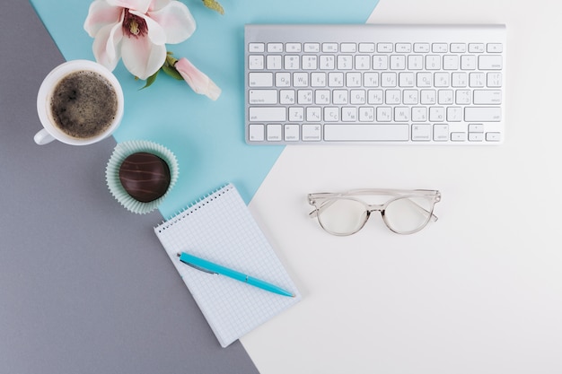 Stylo près de cahier, tasse, biscuit, fleur, lunettes et clavier