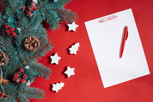 Stylo rouge et bloc-notes sur table rouge décoré d'une branche de sapin. L'arrière-plan du texte.