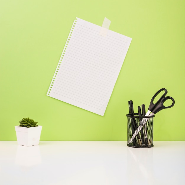 Photo gratuite stylos et ciseaux dans le support près du papier coincé sur le mur vert