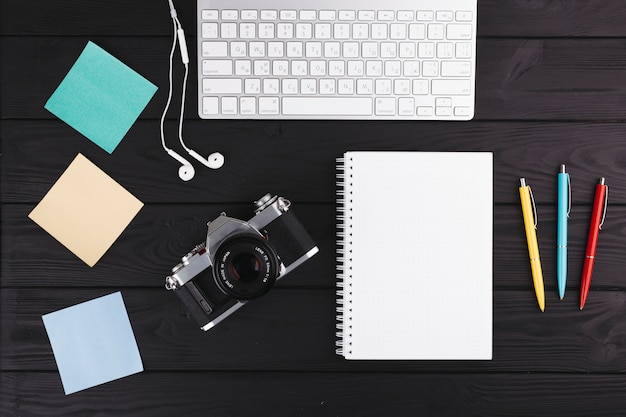 Stylos près de cahier, appareil photo, écouteurs, papiers et clavier