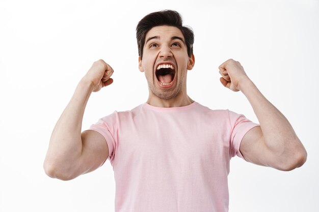 Succès et célébration. Homme excité regardant l'écran, pari gagnant, serrant la main et criant oui, célébrant la victoire, gagnant et triomphant, debout sur fond blanc