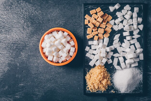 Sucre brun et blanc dans une planche à découper et un bol. mise à plat.