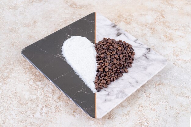 Sucre et grains de café disposés en forme de coeur sur une plaque de marbre