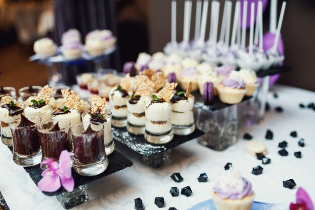 Des sucreries savoureuses recouvertes d&#39;une verrerie violette et blanche servies sur le noir