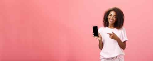 Photo gratuite suggérer ce modèle de téléphone heureux charmante femme afro-américaine aux cheveux bouclés en tenue élégante tenir